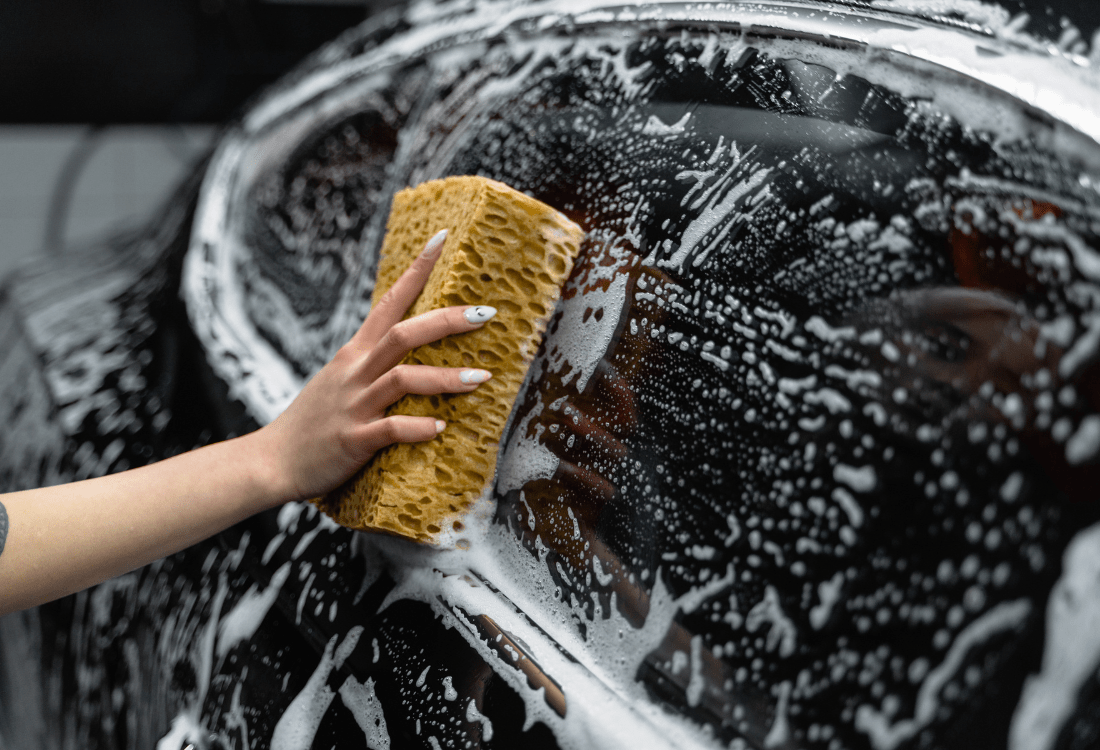 A person using cleaning products and a sponge to clean a car window experiencing the advantages of the car cleaning chemicals market